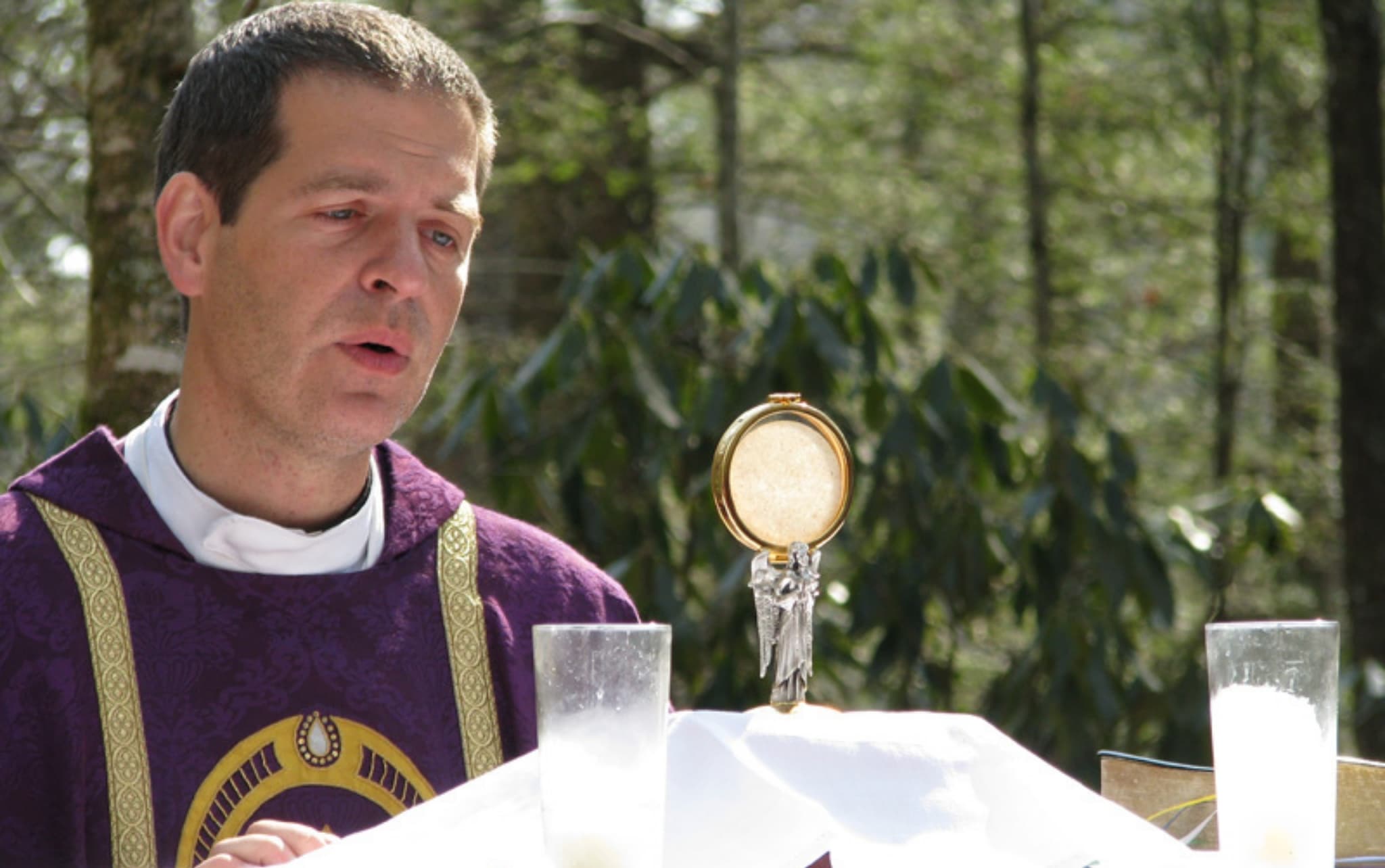 Fr. Henry Kowalczyk SHM in purple chasuble looking at a golden monstrance and on the altar.