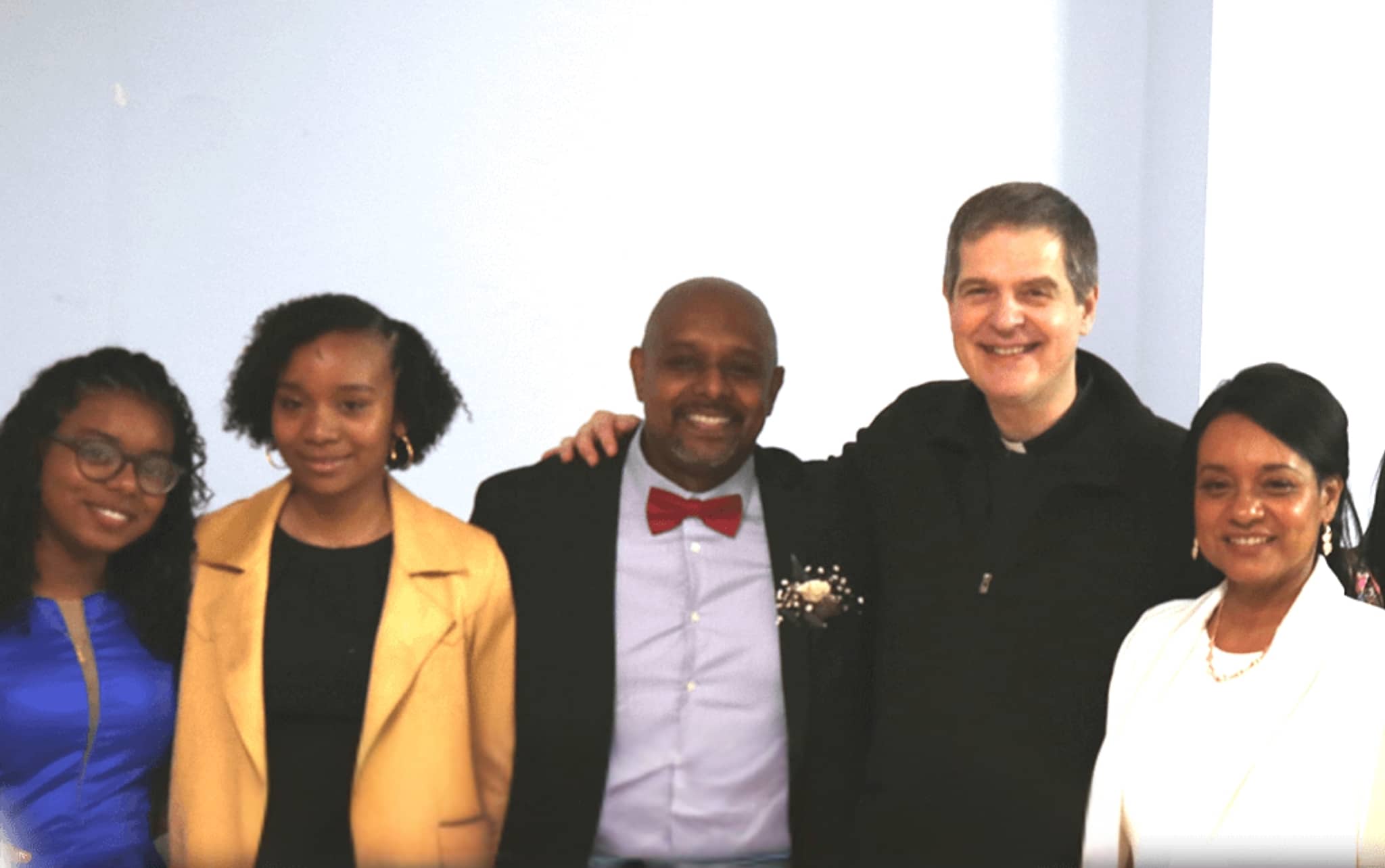 In Our Family Group picture including Fr. Henry Kowalczyk with a family: James, Marina, Isabel, and a friend of theirs; arms around each other;